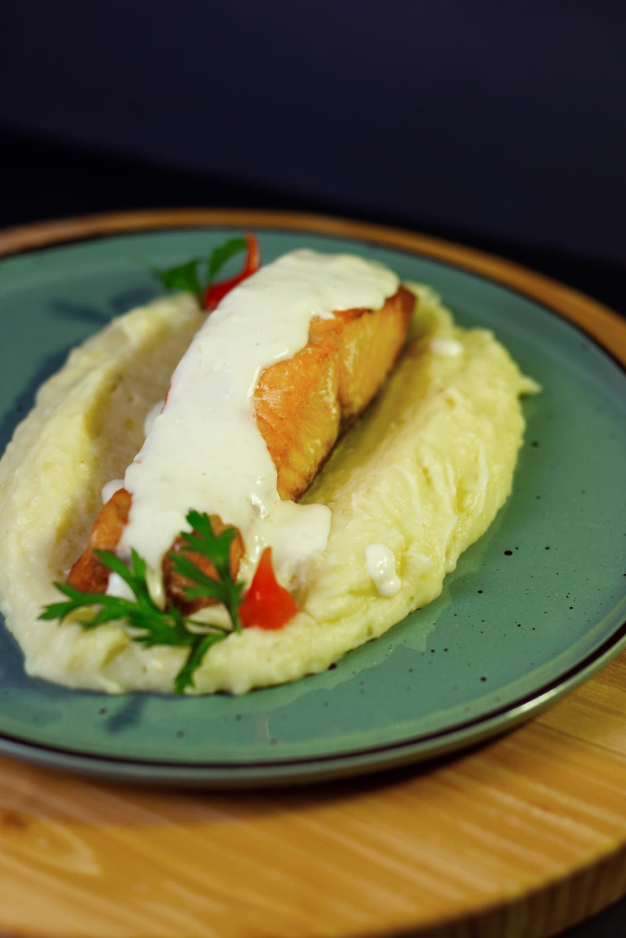 Filé de salmão com molho branco sobre purê em prato verde, decorado com ervas e pimenta