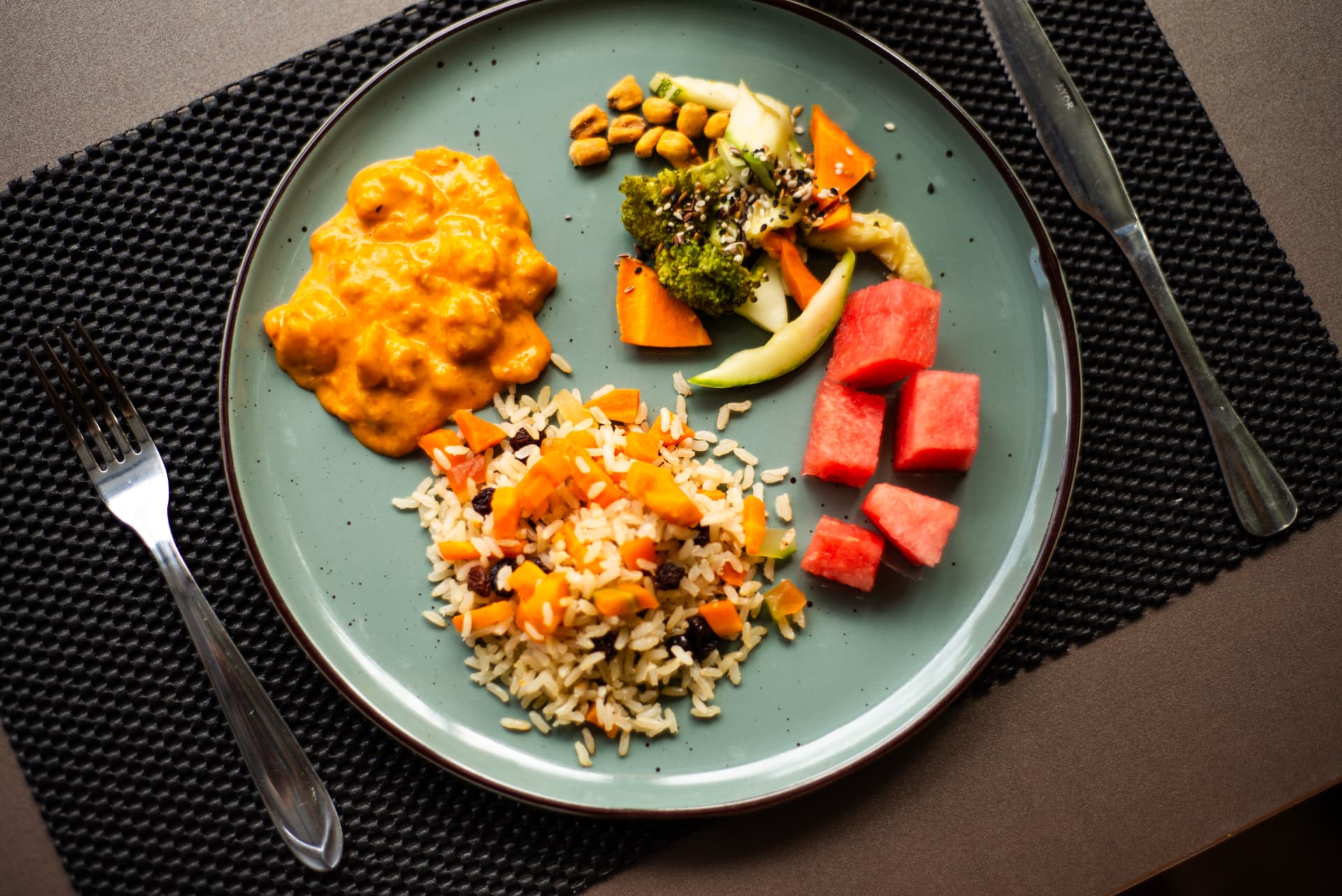 Prato verde visto de cima com arroz, molho cremoso, legumes, salada e cubos de melancia